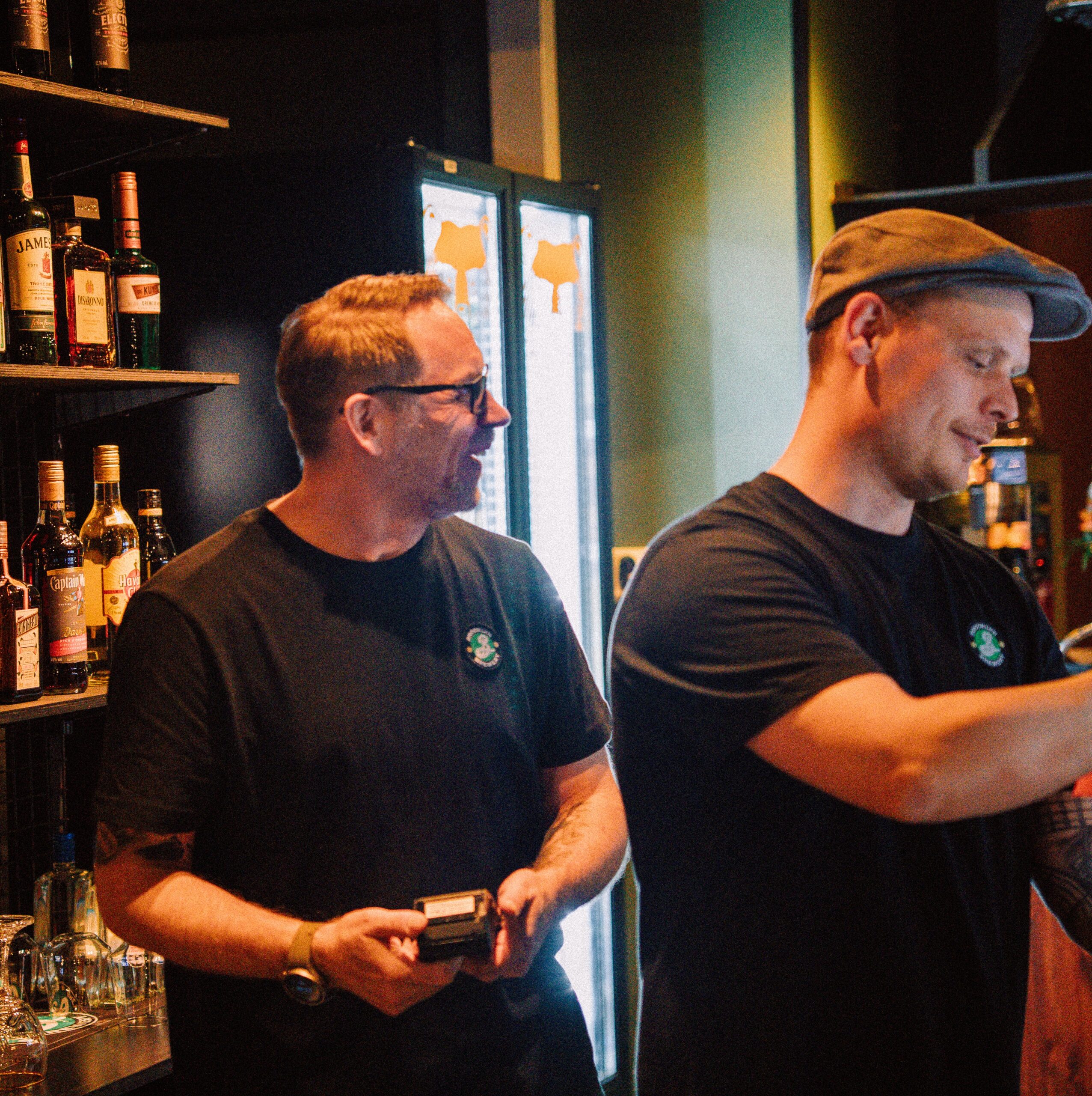 Kaksi hymyilevää miestä töissä baaritiskin takana